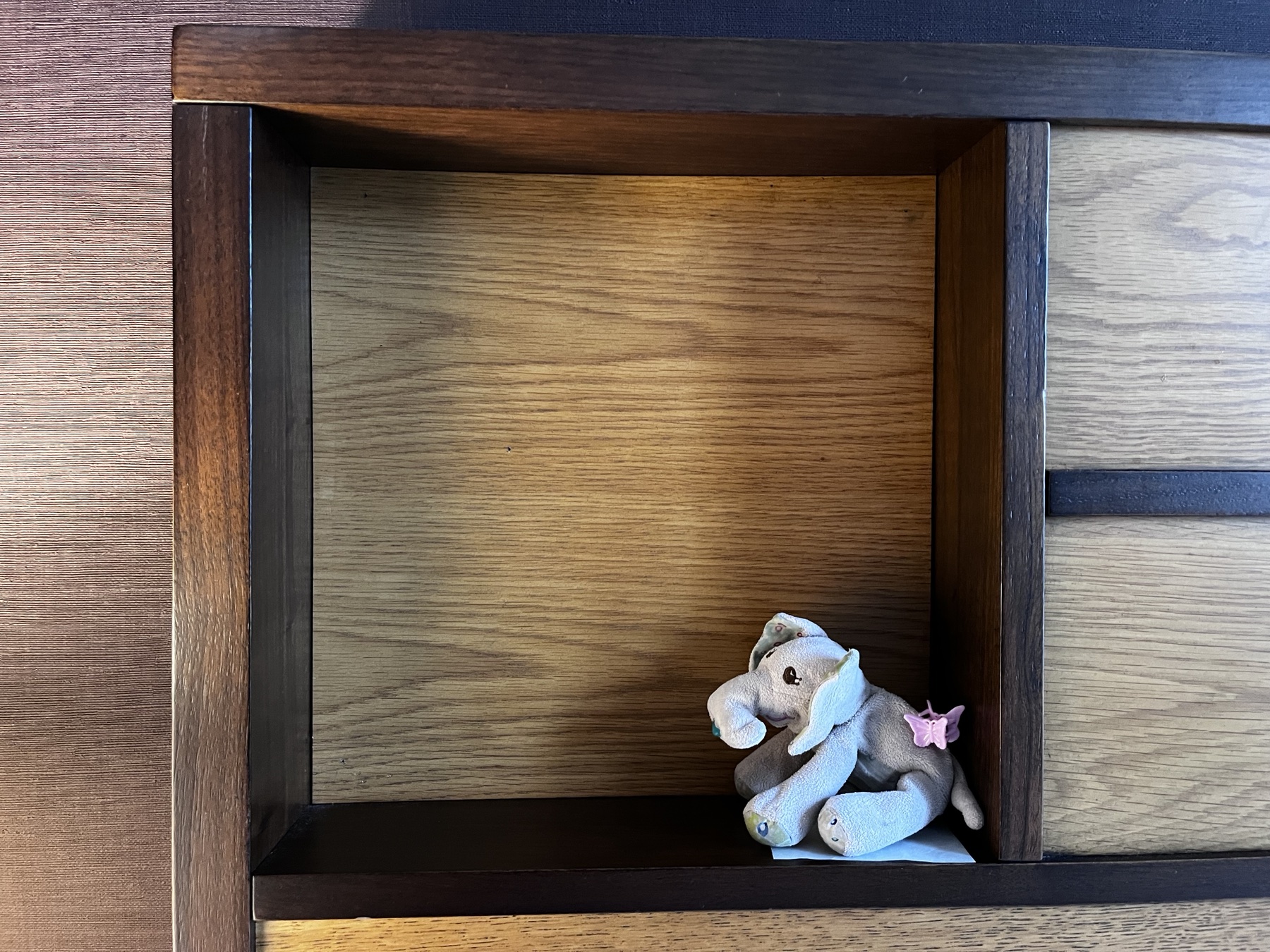 A small stuffed elephant sitting in a wooden alcove
